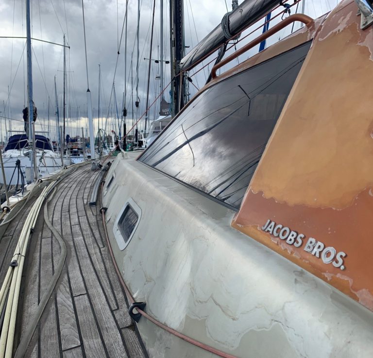 Sailboat docked, with a prominent "Jacobs Bros." sign and cloudy skies overhead.