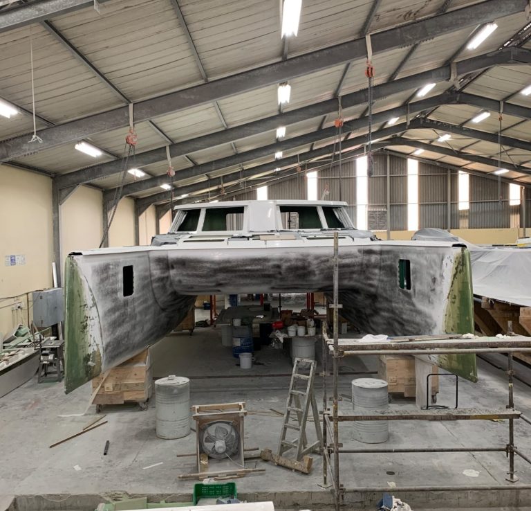 Catamaran in a workshop, with workers and materials visible inside the spacious area.
